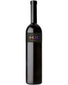 Rotwein Cuvée H21 von Leo Hillinger in einem Weinglas, dunkle Trauben und elegantes Weinglas auf einem Holztisch.