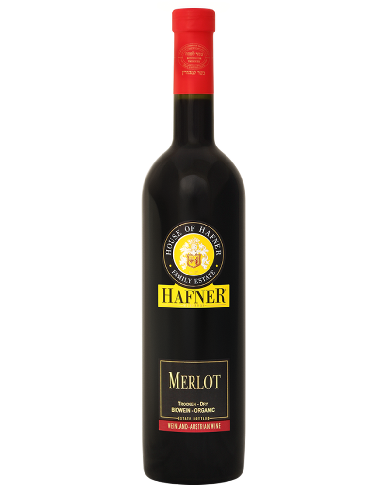 Hafner Merlot "L" 2024 Rotwein in einem Weinglas, dunkle rubinrote Farbe, elegante Flasche im Hintergrund